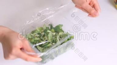 女人用食物胶片在白色桌子上储存食物。 包装产品用透明聚乙烯食品膜辊